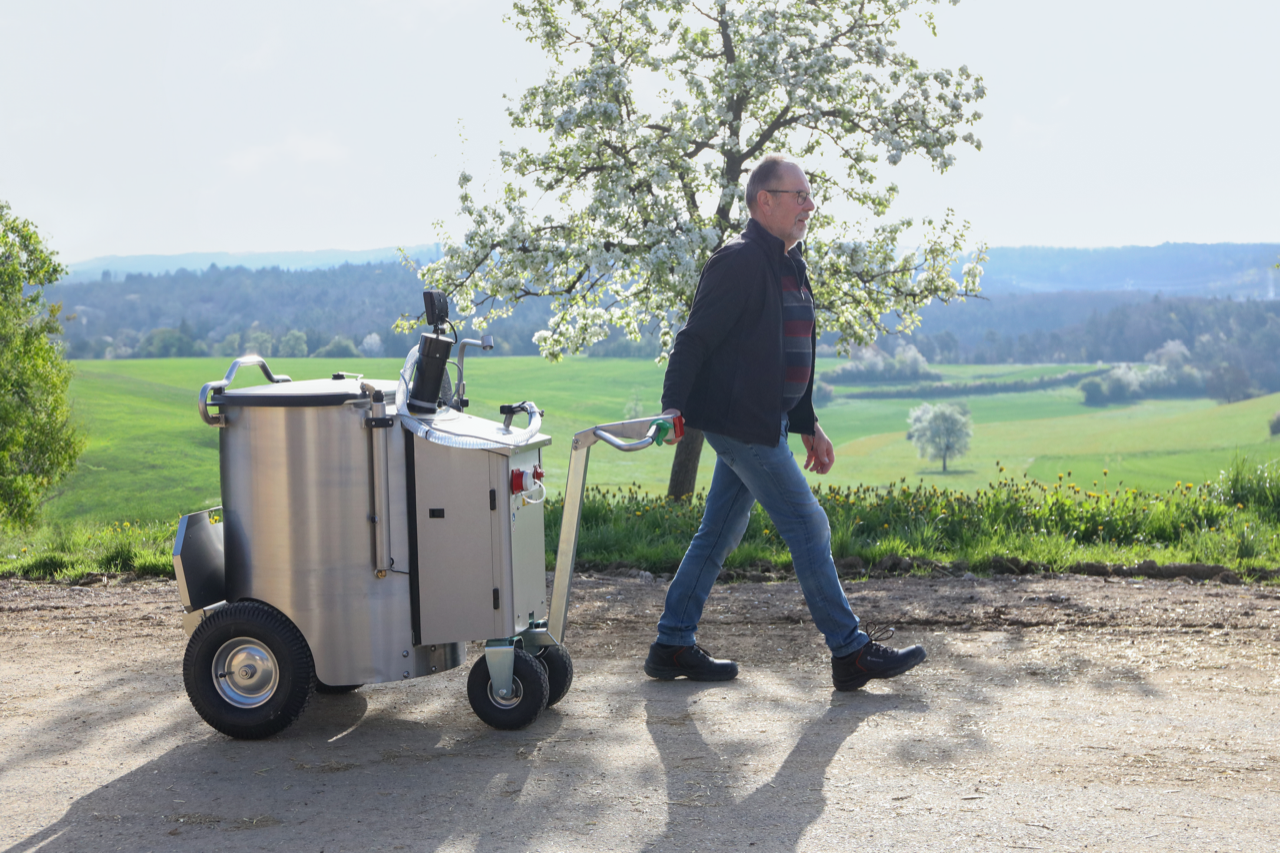 Ein Landwirt zieht das MilchMobil durch eine natürliche Umgebung, umgeben von grüner Landschaft.